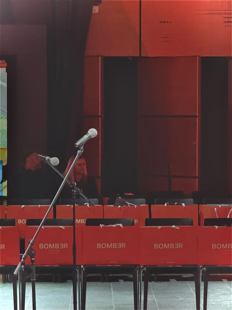 Fotografija scenografije revije BOMBER – Draft Night u Zagrebu s redovima sjedala, narančastim vrećicama i binom