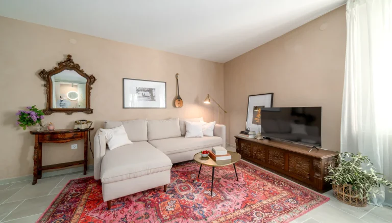 Fotografija dnevnog boravka apartmana u Rovinju s bež mikrocementom, crvenim tepihom i antiknim drvenim detaljima