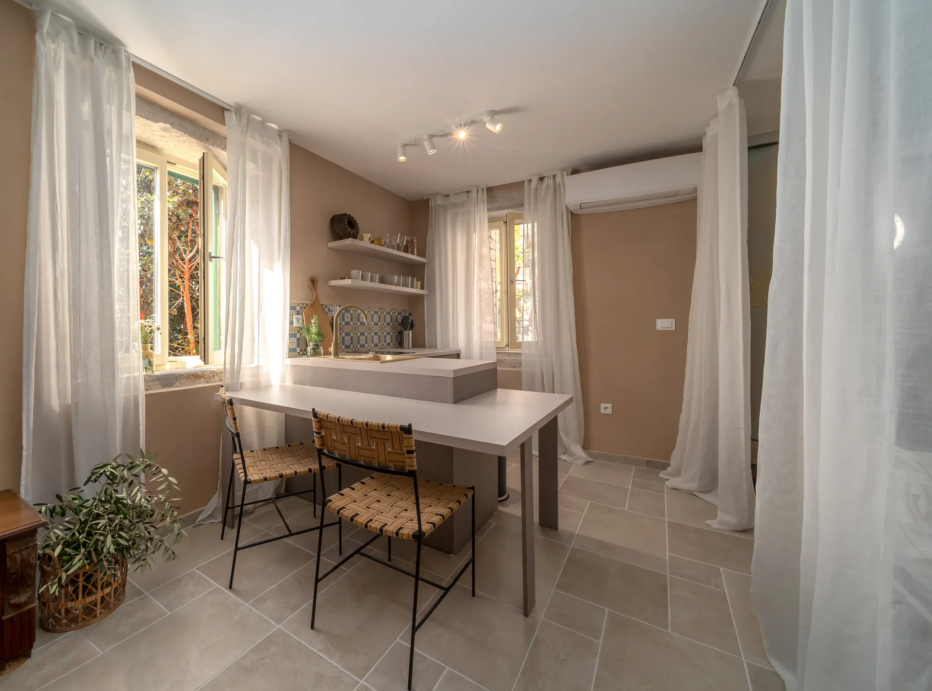 Fotografija kuhinje i blagovaonskog šanka apartmana u Rovinju s bež mikrocementom i pletenim stolicama